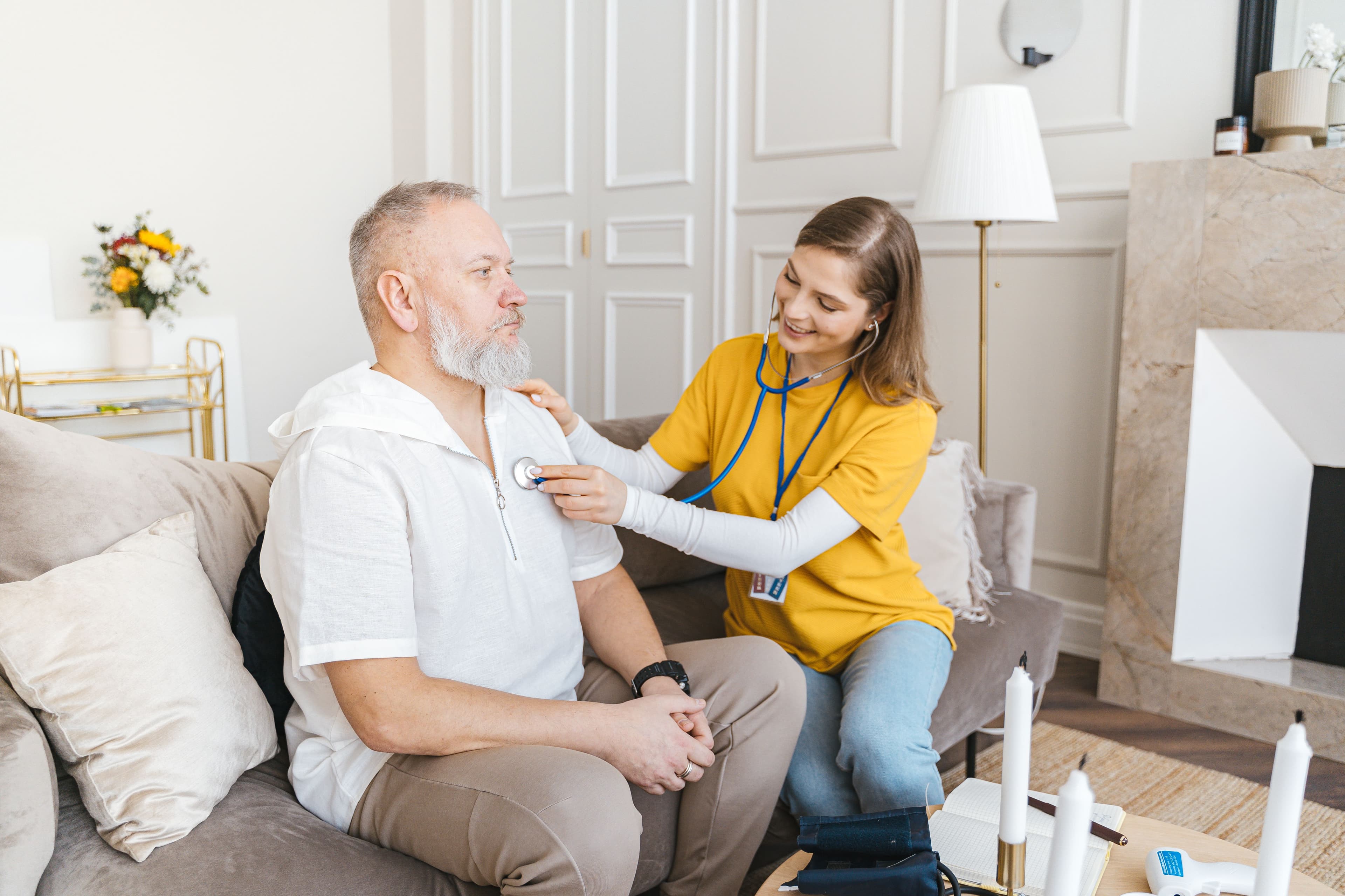 A nurse smiling while checking a patient with a stethoscope during a home visit
